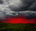 Dramatic stormy clouds and red sunset sky over green field Royalty Free Stock Photo