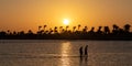 Dramatic sunrise on the Red Sea coast, two men walking through the calm sea in Hurghada, Egypt