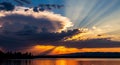 Dramatic sunset with crepuscular rays beaming through dark clouds over a calm lake and distant mountains Keywords Royalty Free Stock Photo