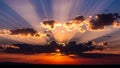Dramatic sunset with crepuscular rays piercing through dark clouds over a silhouetted horizon Royalty Free Stock Photo