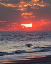 Dramatic sunset over the ocean as the sun dips below the horizon though vibrant clouds.