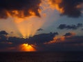 Dramatic sunset over the sea with rays of light emerging from dark illuminated clouds over a calm ocean