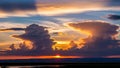 Dramatic sunset sky filled with vibrant orange and yellow clouds casting rays of light over a dark horizon and calm Royalty Free Stock Photo