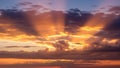 Dramatic sunset sky with vibrant orange and yellow clouds, illuminated by crepuscular rays beaming through dark storm Royalty Free Stock Photo