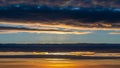 Dramatic sunset sky with layered dark blue and orange clouds illuminated by golden sunlight breaking through Royalty Free Stock Photo