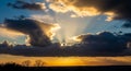 Dramatic Sunset Sky with Sun Rays Breaking Through Dark Clouds Over Silhouetted Trees and Horizon Keywords: sunset Royalty Free Stock Photo