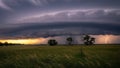 Dramatic supercell thunderstorm with lightning strike over a grassy field at sunset Royalty Free Stock Photo