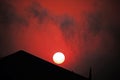 Setting sun with glowing red wispy cloud visible above a slanted roof. Royalty Free Stock Photo