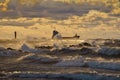 Vessel leaving a harbor and passing lighthouse and pier, breaking through stormy waves, lit by the yellow sunset light