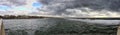 Dramatic weather panorama over the sea threatening waves crashing at the shore with overcast sky and sunbeams on the water Royalty Free Stock Photo