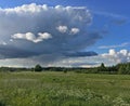 Dramatic clouds on green meadow with forest horizon
