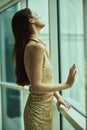 Dramatic woman in a designer glittery evening dress standing by the window looking out over the city, hotel party dress