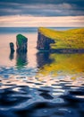 Drangarnir cliffs reflected in the calm waters of Atlantic ocean.