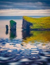 Drangarnir cliffs reflected in the calm waters of Atlantic Ocean.