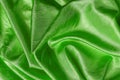 Draped shiny wrinkled silk of kelly green color texture. Background of folded emerald green satin cloth. Elegant luxury crumpled