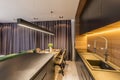 Drapes hanging in modern kitchen interior with black shelves and countertop, wooden table and chairs