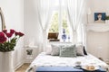 Drapes at window above bed with cushions in white bedroom interior with poster and roses. Real photo Royalty Free Stock Photo