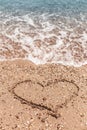 Drawing of a heart on the sand on the beach and wave with foam. Sea travel and holiday. Royalty Free Stock Photo