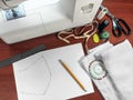 Drawing of a pattern of a medical face mask lies on the surface of a brown wooden table near the sewing machine and other