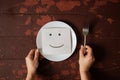 A drawing of a smile lies on a white empty plate on a wooden table and female hands hold the plate Royalty Free Stock Photo
