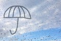 The drawing of an umbrella drawn by a finger on the misted glass. Window glass with raindrops against a blue sky and sun