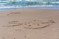 Drawn smile symbol and word smile written in beach sand with blue sea and waves in background Royalty Free Stock Photo