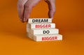 Dream and do bigger symbol. Concept words `Dream bigger do bigger` on wooden blocks on a beautiful orange background. Businessma