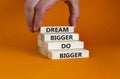 Dream and do bigger symbol. Concept words `Dream bigger do bigger` on wooden blocks on a beautiful orange background. Businessma