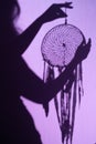 Dreamcatcher in silhouette of a woman\'s hand on a purple background.