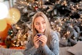 Dreamful cute teen girl near Christmas tree with cup of cacao. Kid wearing pajama dreaming near tree in the morning Royalty Free Stock Photo