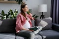 Dreamful happy smiling young pregnant woman sitting on comfortable sofa and writing to diary or notebook at home. Beautiful future Royalty Free Stock Photo