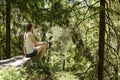 Dreaming beautiful girl sitting on a stone surrounded by coniferous forest on a sunny day Royalty Free Stock Photo