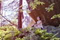 Dreaming beautiful girl sitting on a stone under a rock surrounded by forest on a sunny day Royalty Free Stock Photo