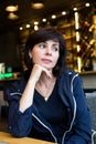 A dreaming brunette woman is sitting at a table in a cafe