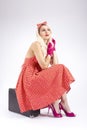 Dreaming Cute Charming Blond Girl in Pin-up Style Posing In Red Polkadot Dress With Suitcase Against White
