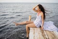 Dreaming girl sitting on the pier of the forest and the river in the background. Sad girl depressed on a bridge by the Sea Royalty Free Stock Photo