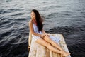 Dreaming girl sitting on the pier of the forest and the river in the background. Sad girl depressed on a bridge by the Sea Royalty Free Stock Photo