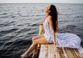 Dreaming girl sitting on the pier of the forest and the river in the background. Sad girl depressed on a bridge by the Sea Royalty Free Stock Photo