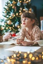 Dreaming little girl writing a letter near Christmas tree Royalty Free Stock Photo