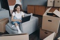 Pensive girl planning house interior design on laptop, sitting with boxes. Moving, flat renovation Royalty Free Stock Photo