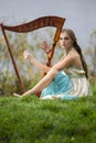Dreaming sensual female harpist in light dress playing music in park outdoor