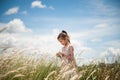 Dreaming small girl wearing dress among the meadow on blue cloudy sky background