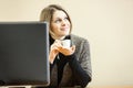 Dreaming woman with coffee cup is behind computer monitor