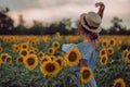 Dreaming young woman in blue dress and hat dancing in a field of sunflowers at summer, view from her back. Looking forward Royalty Free Stock Photo