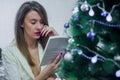 Dreaming young woman sitting chair and reading book in front of Christmas tree. Royalty Free Stock Photo