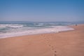 Dreamlike seascape in light blue and pink colors. Ocean, wide sandy beach, foot prints on sand, and silhouette of walking man