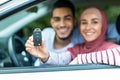 Dreams come true. Glad happy young arab husband and wife in hijab customers show keys at new car, close up