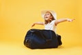 Dreams of travel. A little child girl sits in a suitcase and plays the pilot of the plane and the traveler. Yellow background