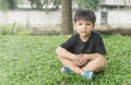 Dreamy Asian boy is sitting on the grass in the park