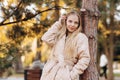 Dreamy beautiful blond girl fixing her hair with her hand, wearing a black sweater and a beige raincoat, standing leaning against Royalty Free Stock Photo
